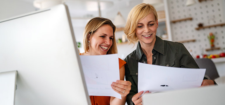 Two professional women with sheets of paper at a computer