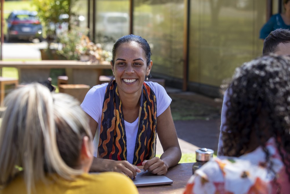 Educator sitting in an outdoor education and care setting with other educators